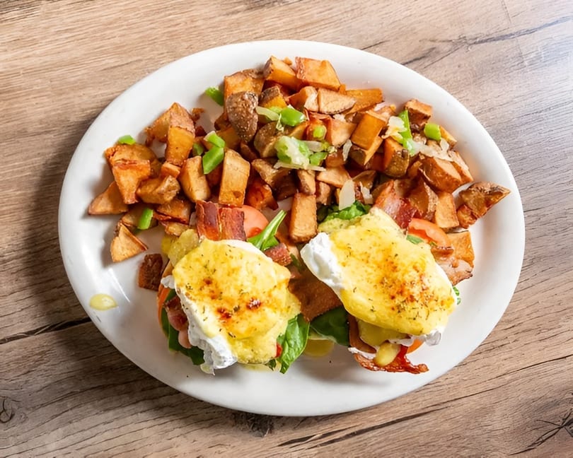 Eggs Benedict with crispy bacon, spinach, and tomatoes, served with a side of seasoned home fries.
