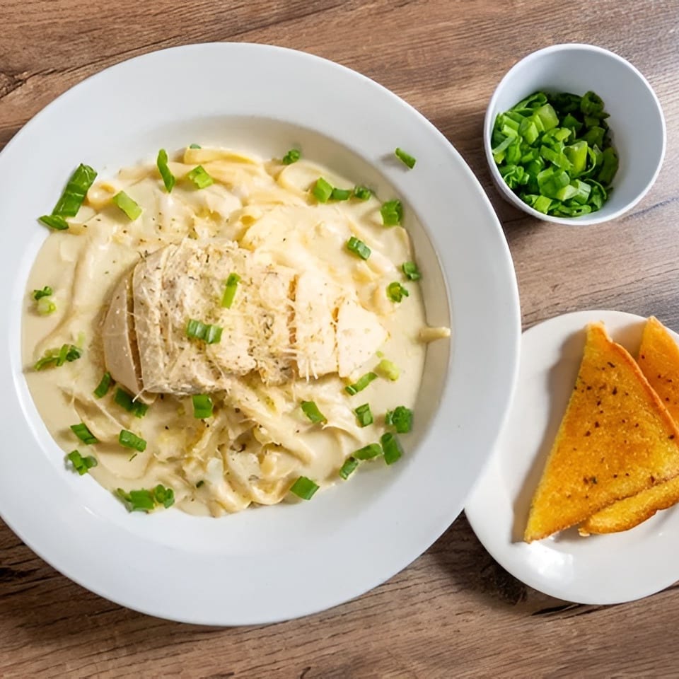 Creamy chicken pasta with green onions and garlic bread on a wooden table.