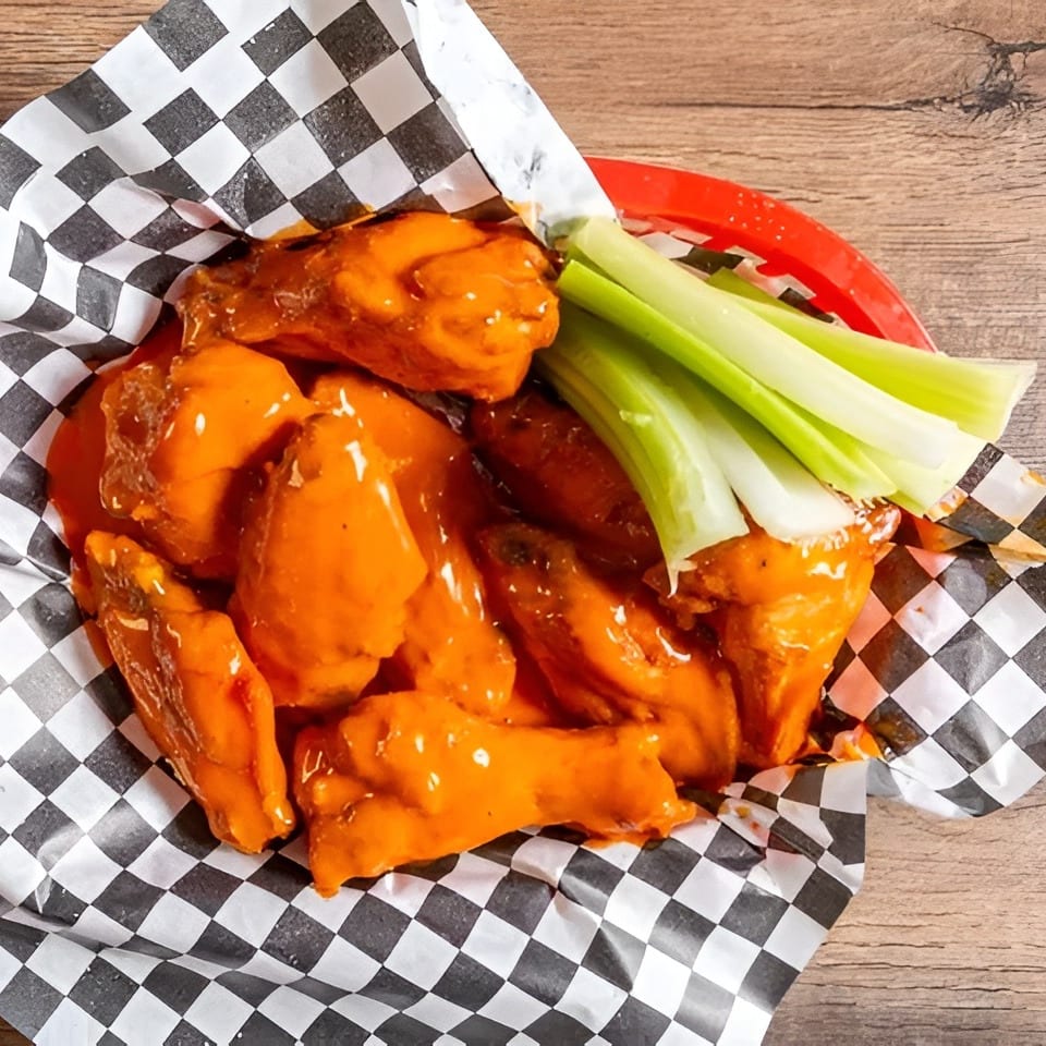 Buffalo chicken wings with celery sticks in a red basket lined with checkered paper.