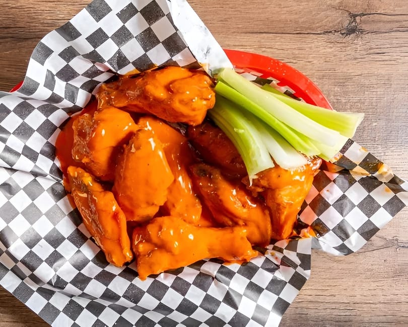 Buffalo chicken wings with celery sticks in a red basket lined with checkered paper.