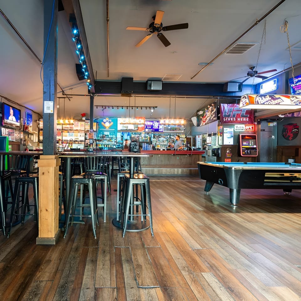A lively bar interior with a long bar, high-top tables, stools, and a pool table.