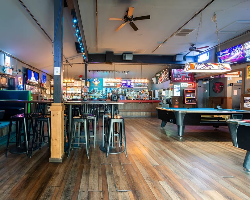 A lively bar interior with a long bar, high-top tables, stools, and a pool table.