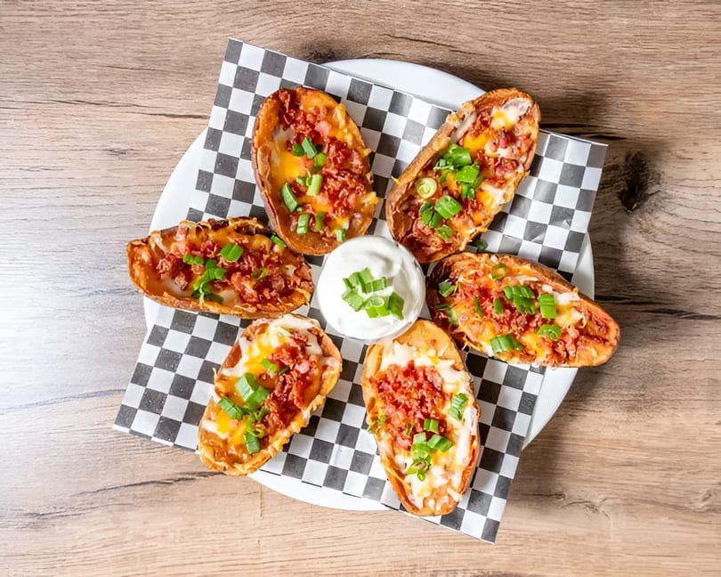 Six potato skins filled with melted cheese, bacon bits, and green onions, served with sour cream.