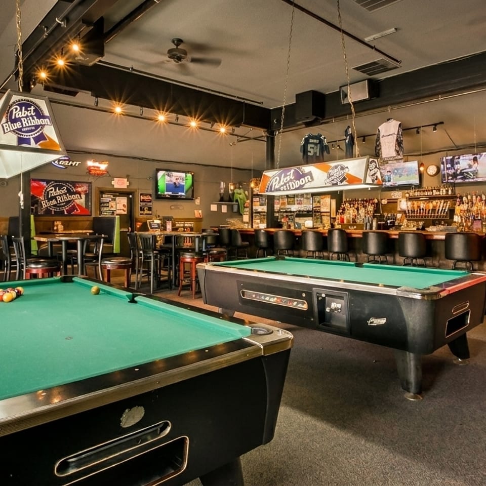 A lively bar interior with two pool tables, a fully stocked bar, and sports memorabilia.